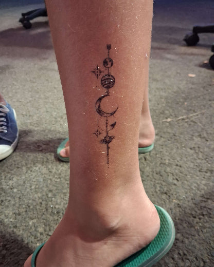 tatouage temporaire 10 jours dimension 7cm représente une fine enfilade de lunes et planetes. tatouage situé sur la cheville en hauteur. photo cinema-tattoo.com été 2026